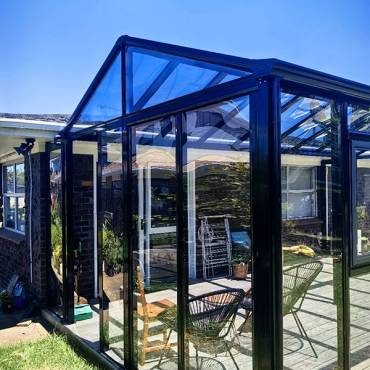 A custom black aluminum sunroom built on an Auckland backyard deck, creating a modern and comfortable outdoor living space.