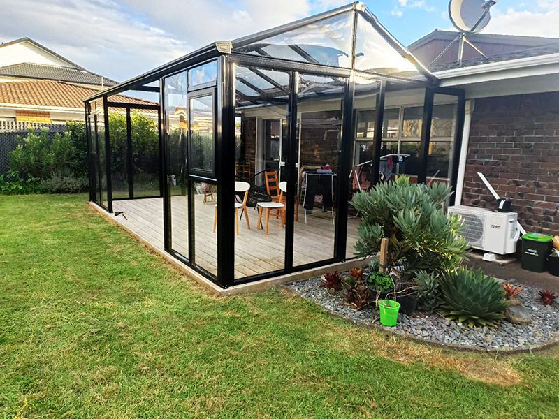 A custom black aluminum sunroom built on an Auckland backyard deck, creating a modern and comfortable outdoor living space.