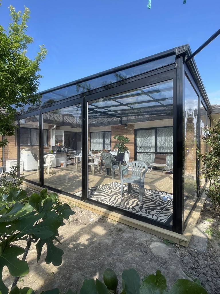 A custom black aluminum sunroom built on an Auckland backyard deck, creating a modern and comfortable outdoor living space.